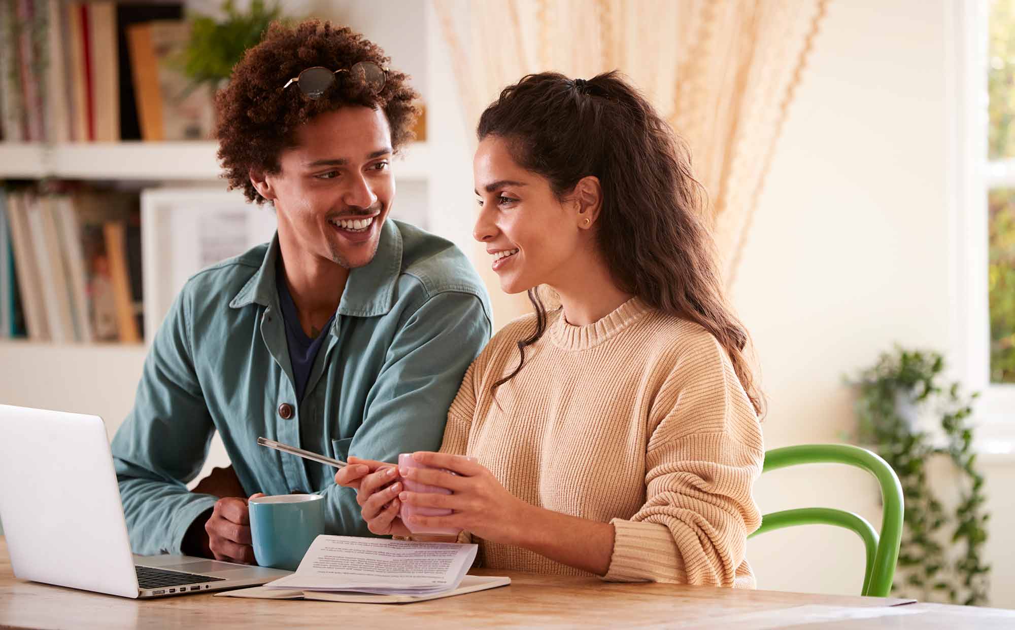 Couple sitting together smiling looking at a laptop with some bills on the table