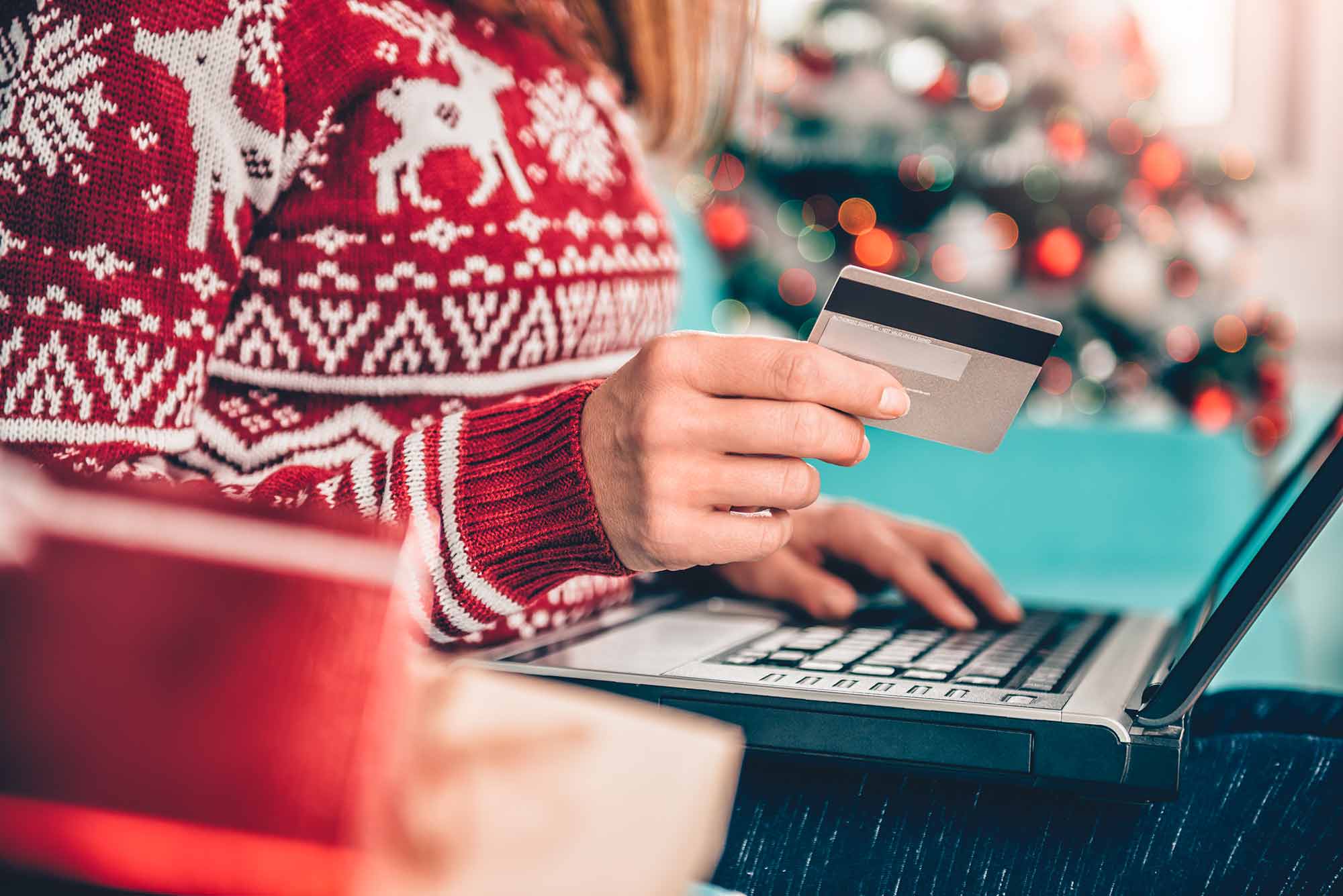 Woman in a red holiday sweater with a laptop and credit card
