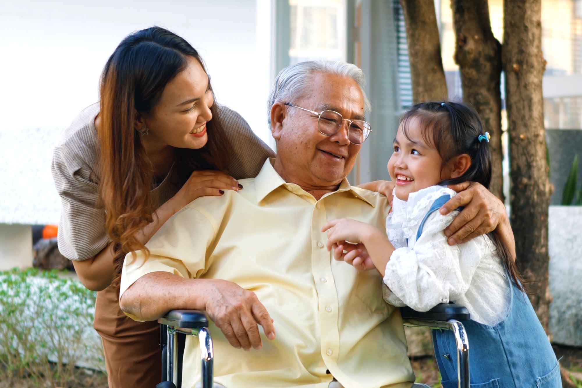 A grandfather in a wheelchair with his daughter and granddaughter smiling