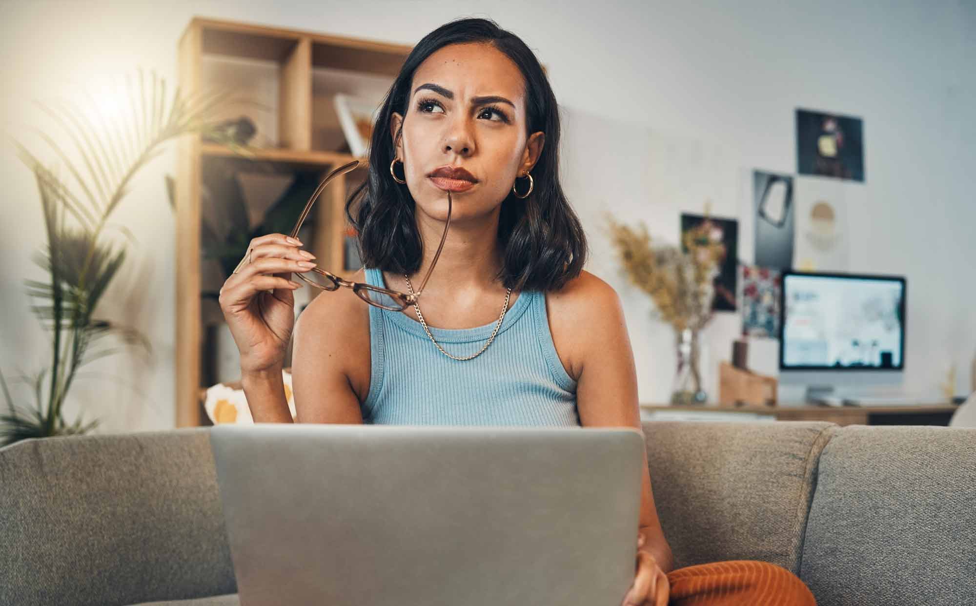 Woman sitting on the couch in her living room thinking with her glasses in her hand