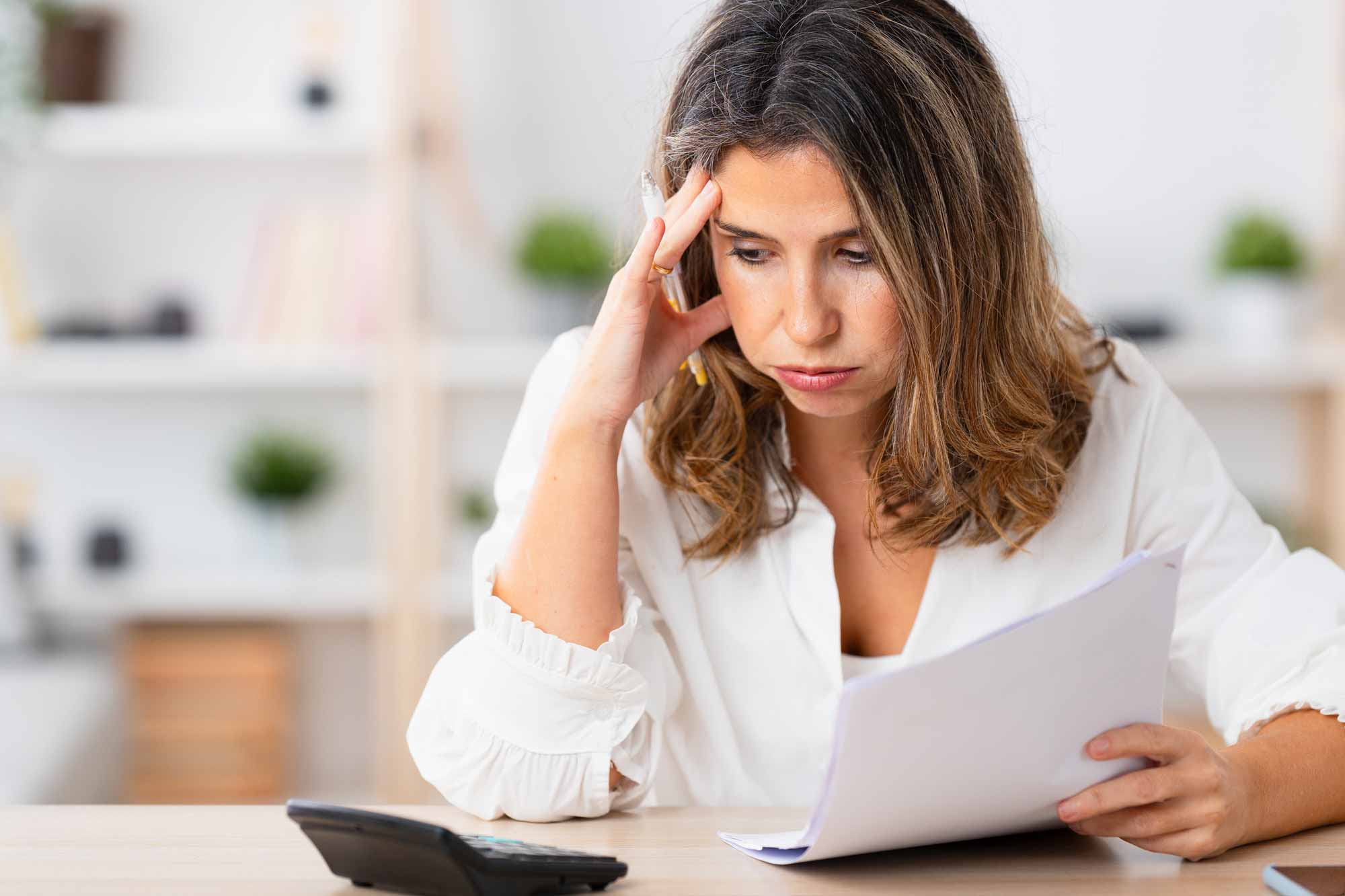 Woman looking at some papers and using a calculator, looking worried