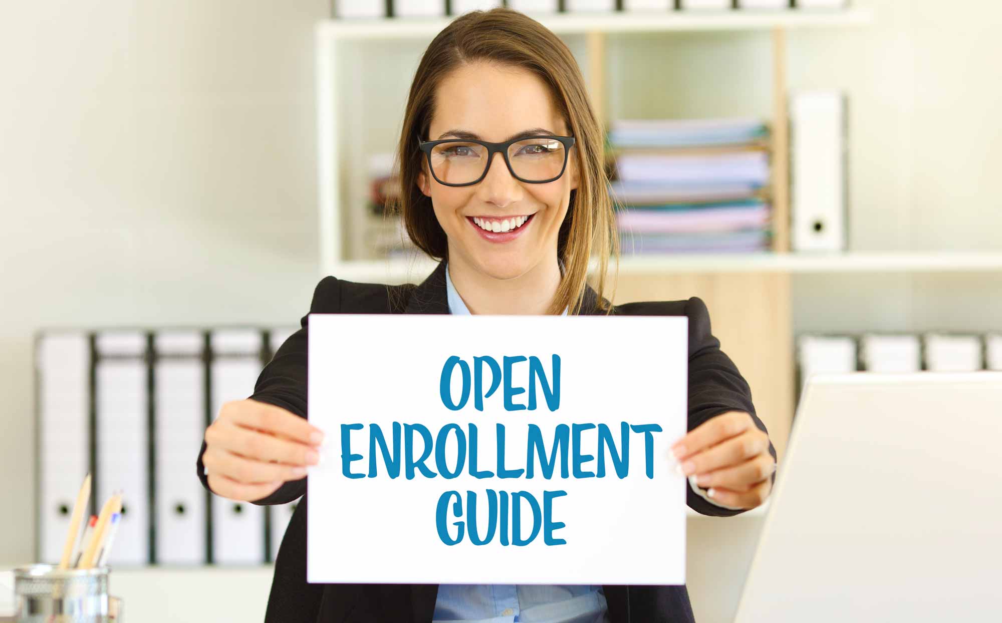 Smiling HR woman in glasses holding a sign that reads: Open Enrollment Guide