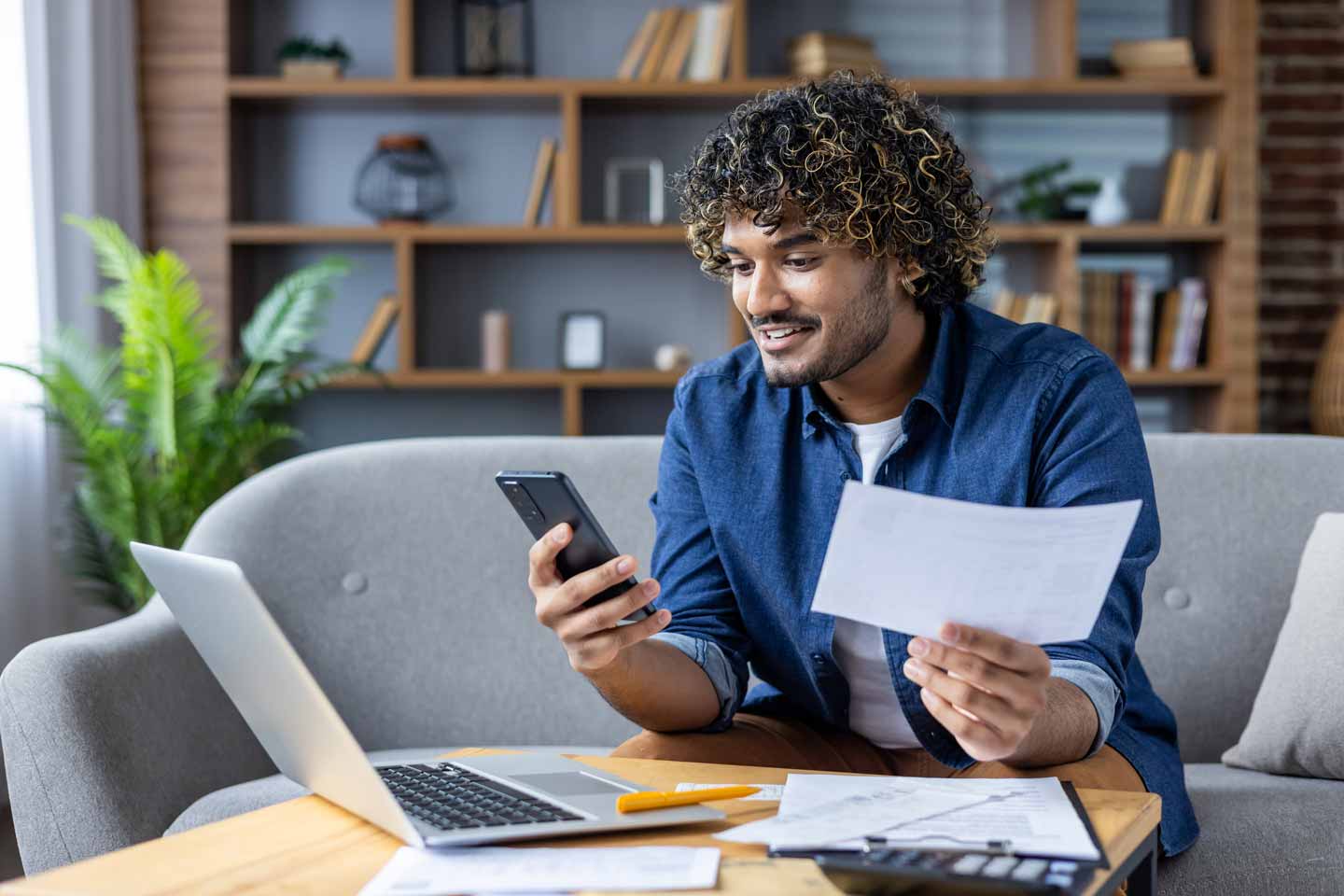 Young man sitting on his couch surrounded by financial papers
