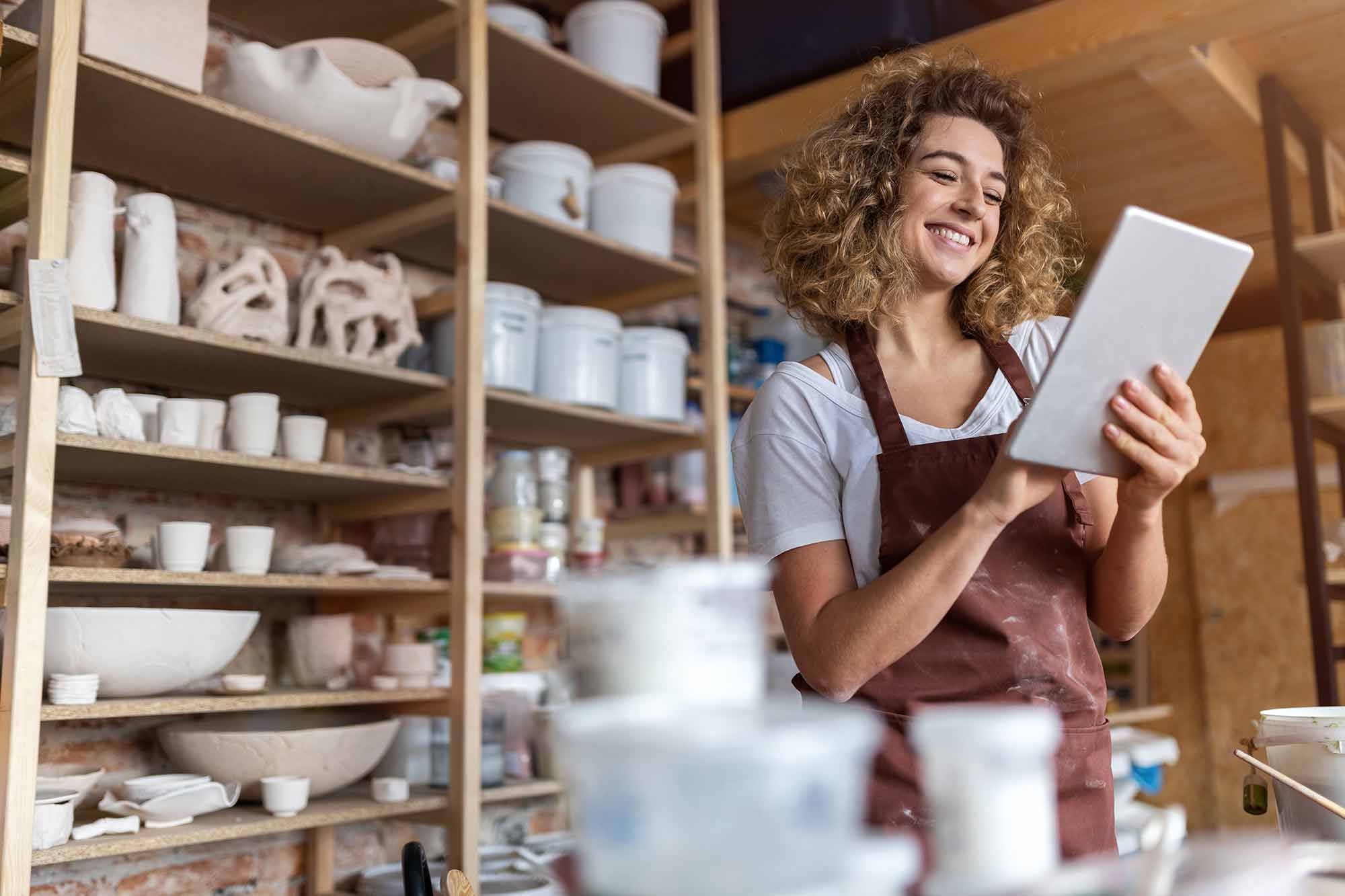 Woman business owner at her pottery shop smiling behind the counter and looking at a tablet