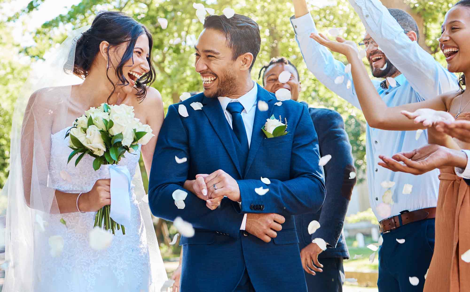 Young couple smiling after their wedding as guests toss flower petals