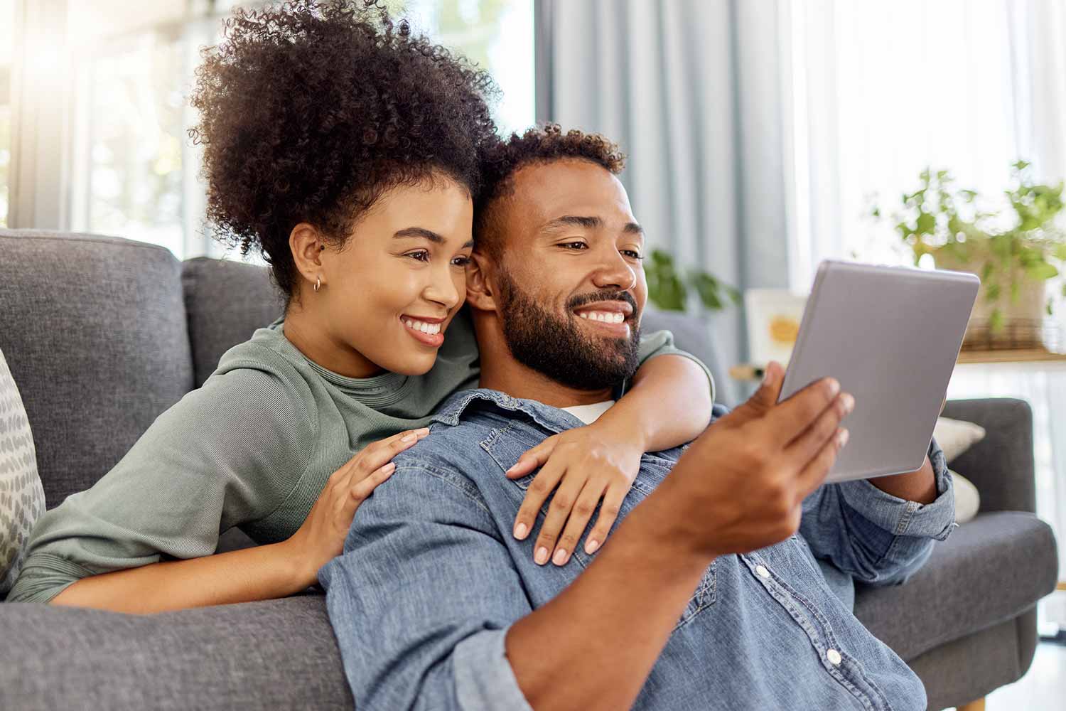 A couple looking at their finances on an ipad together in their home on the couch
