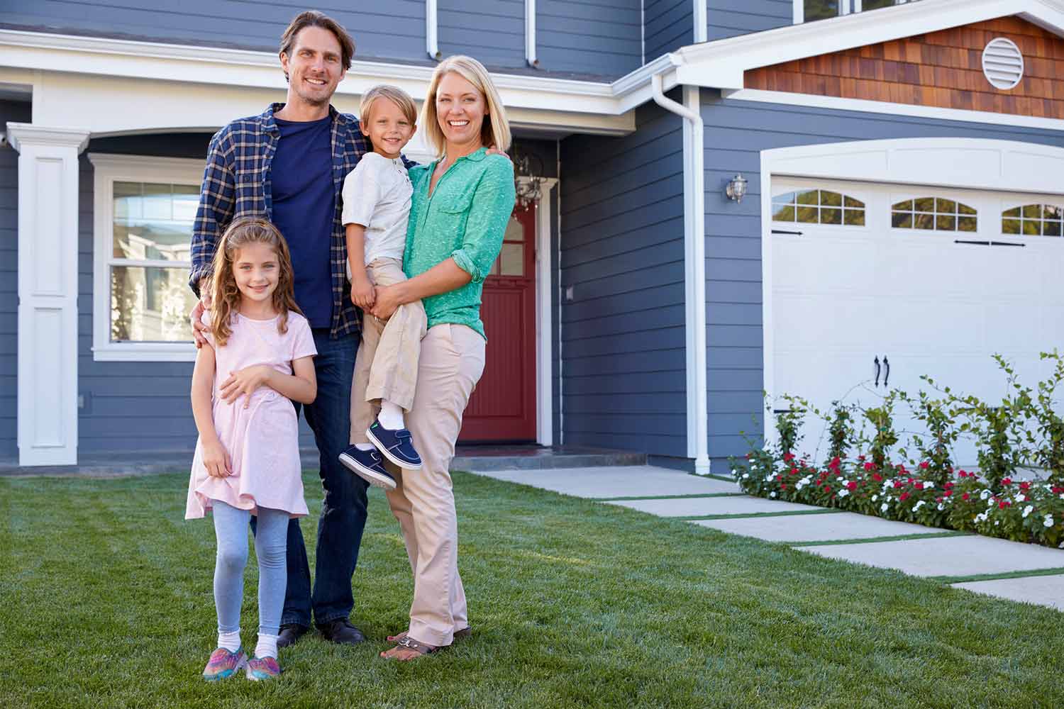 A young couple and their two young children standing on the lawn in front of their home