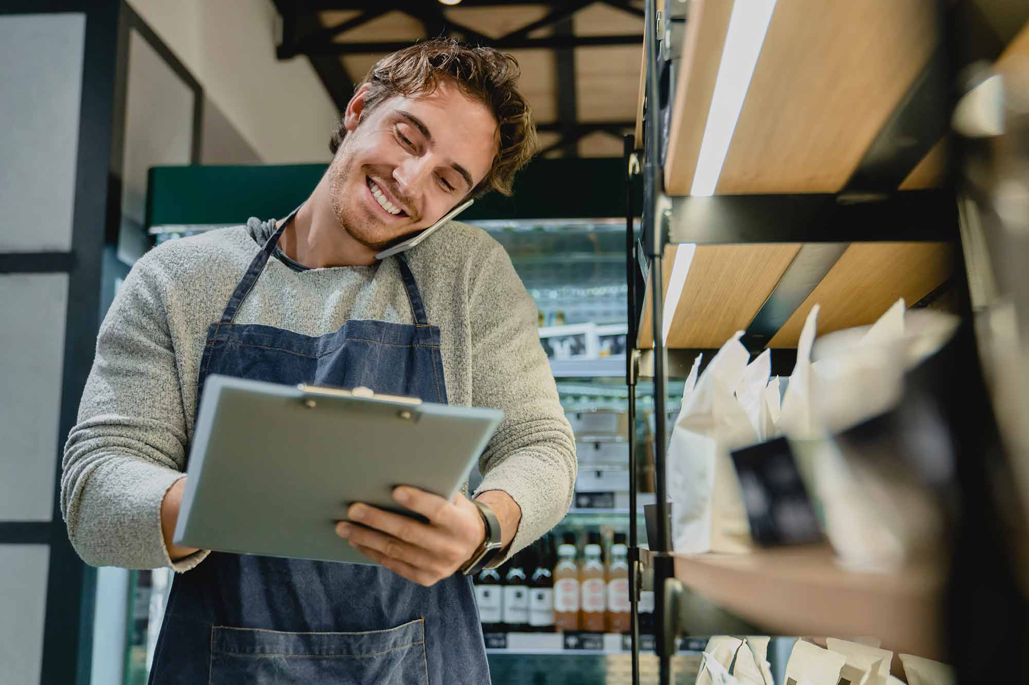 A business owner in an apron on the phone taking inventory or making an order