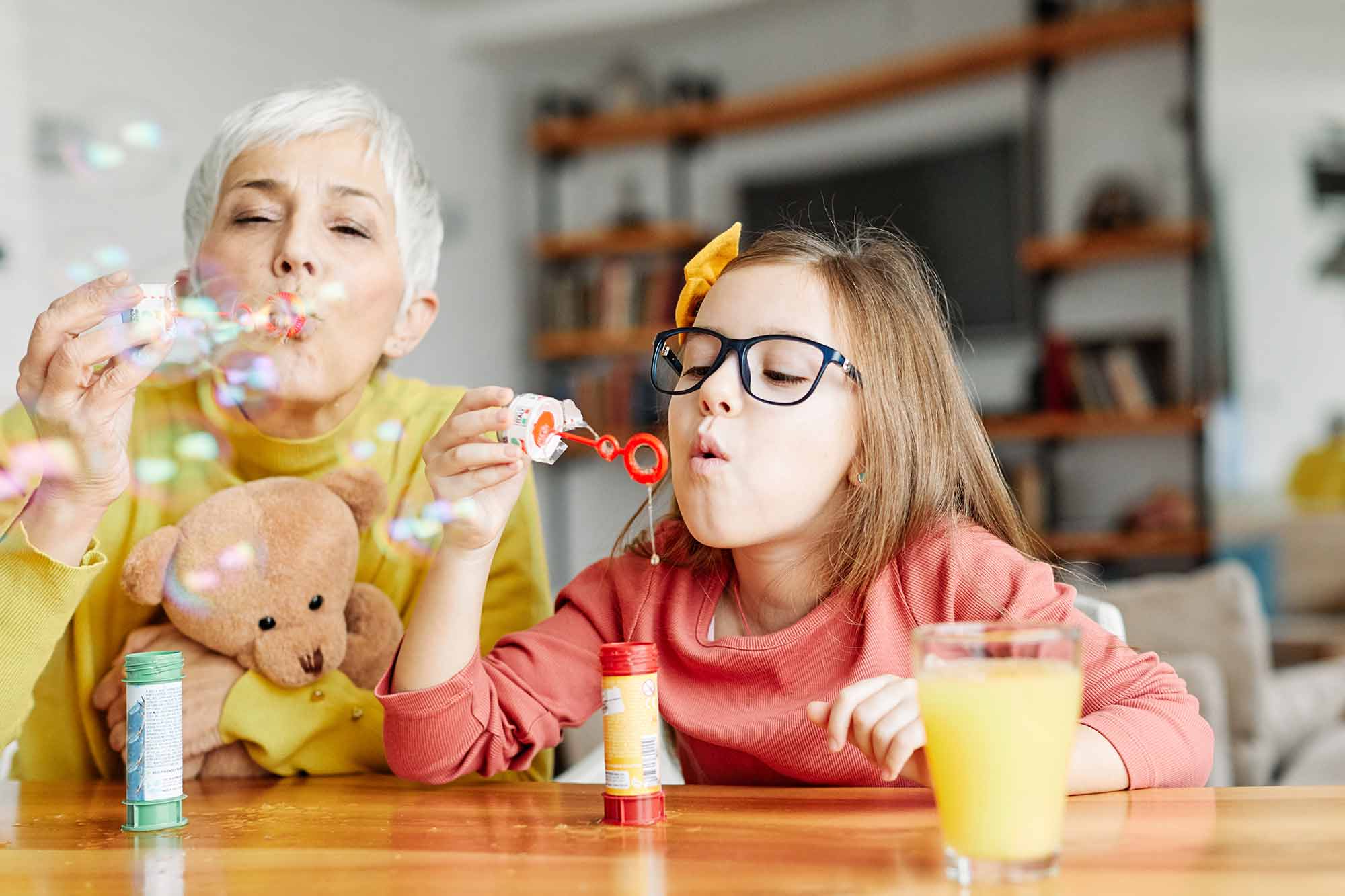 A grandmother and granddaughter blowing bubbles together at the kitchen counter