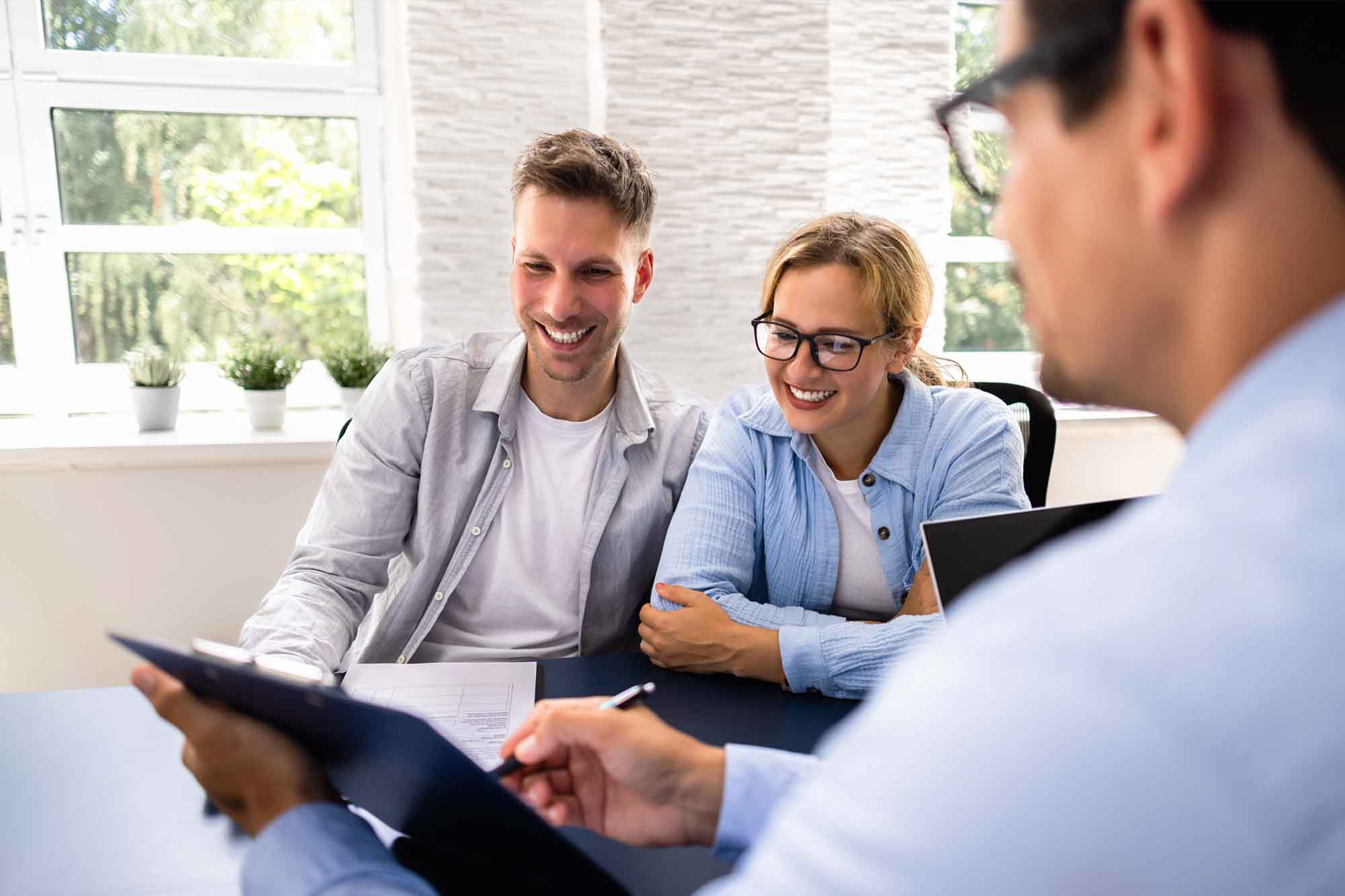 A younger couple smiling at a financial advisor while he explains something to them.