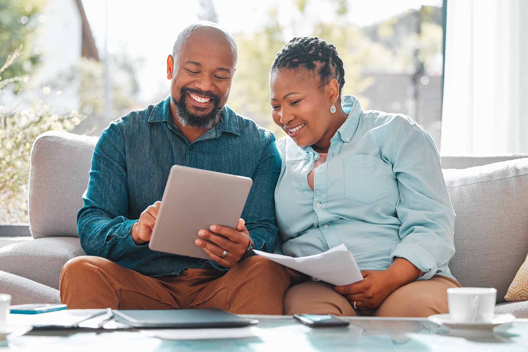 A couple sitting on their couch happily looking at their finances with papers spread out on the coffee table.