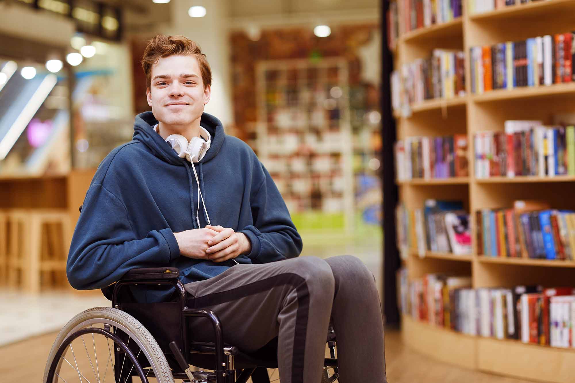 A young hansom boy in a wheel chair with headphones around his neck smiling
