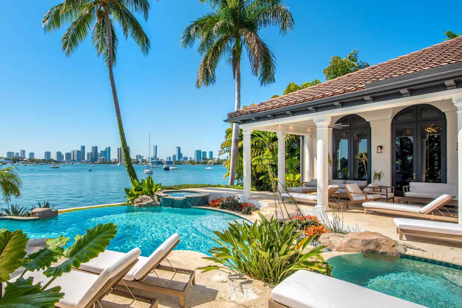A luxurious vacation house someplace tropical with a waterfront pool and palm trees.