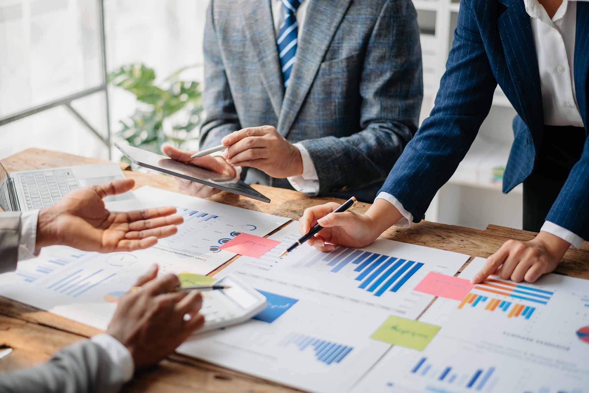 A group of professionals in suits around a table looking at financial charts